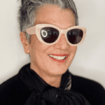 Smiling person wearing sunglasses and black scarf.